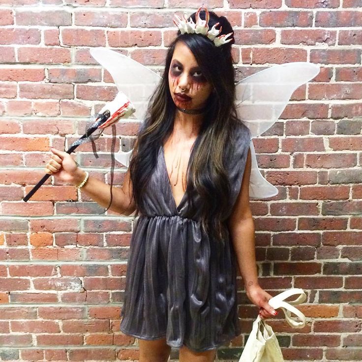 a woman dressed as a fairy with makeup and hair holding scissors in one hand while standing next to a brick wall