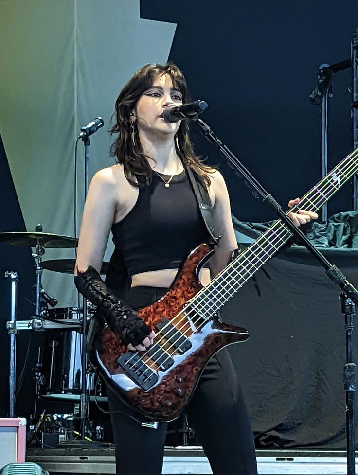 a woman holding a guitar while standing in front of a microphone