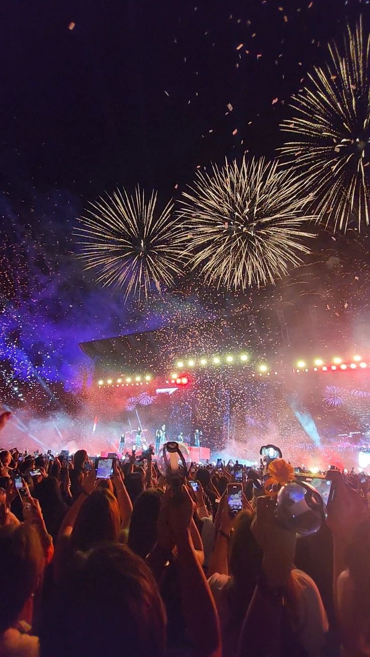 fireworks are lit up in the night sky above a crowd at an outdoor music festival