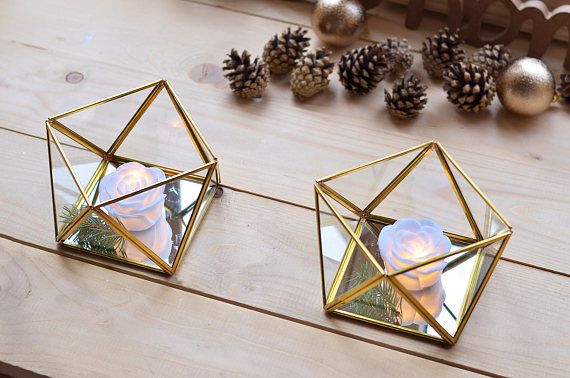 two gold geometric mirrors sitting on top of a wooden table next to pine cones and candles