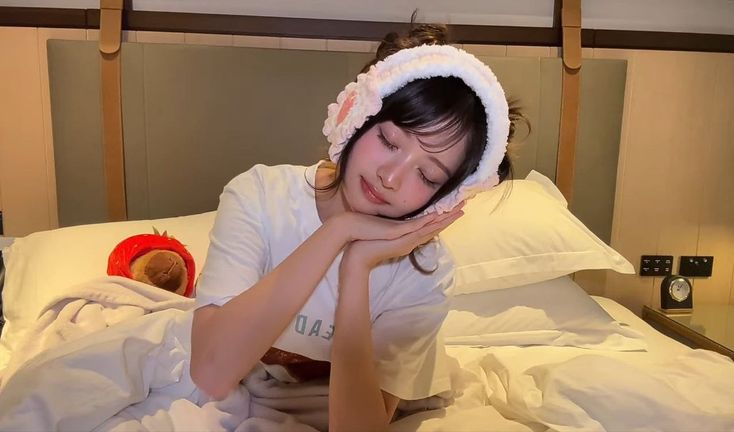 a woman laying in bed with a teddy bear under her blanket and wearing a bonnet