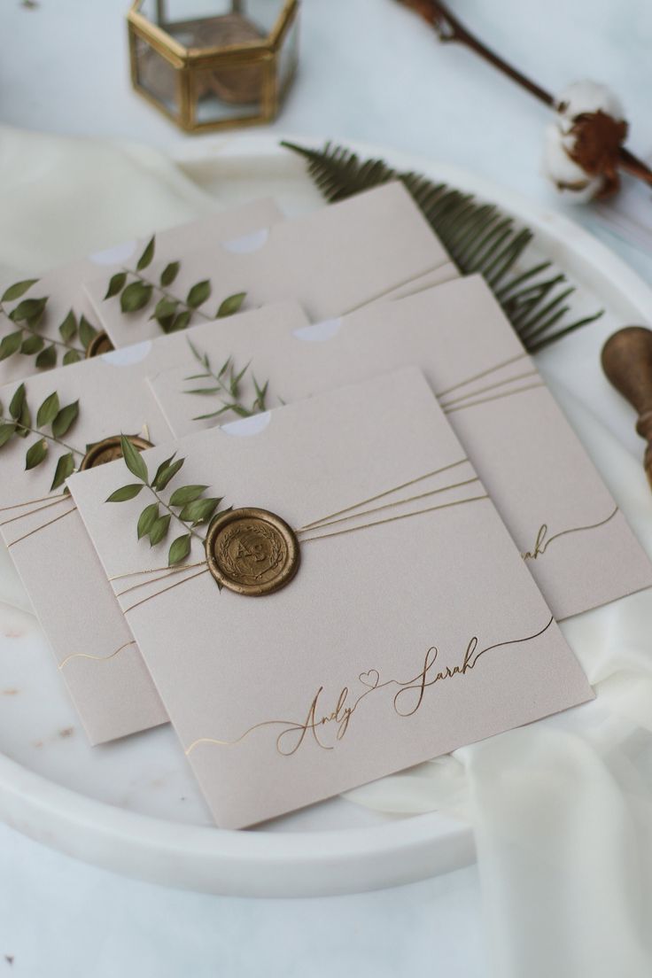 wedding stationery with wax stamp and greenery on white paper laid out on a plate