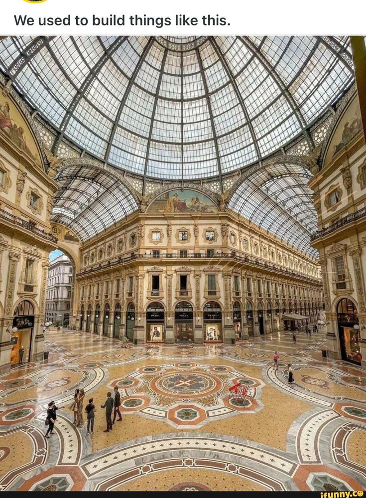 the inside of a building with many people walking around it and lots of glass on the ceiling