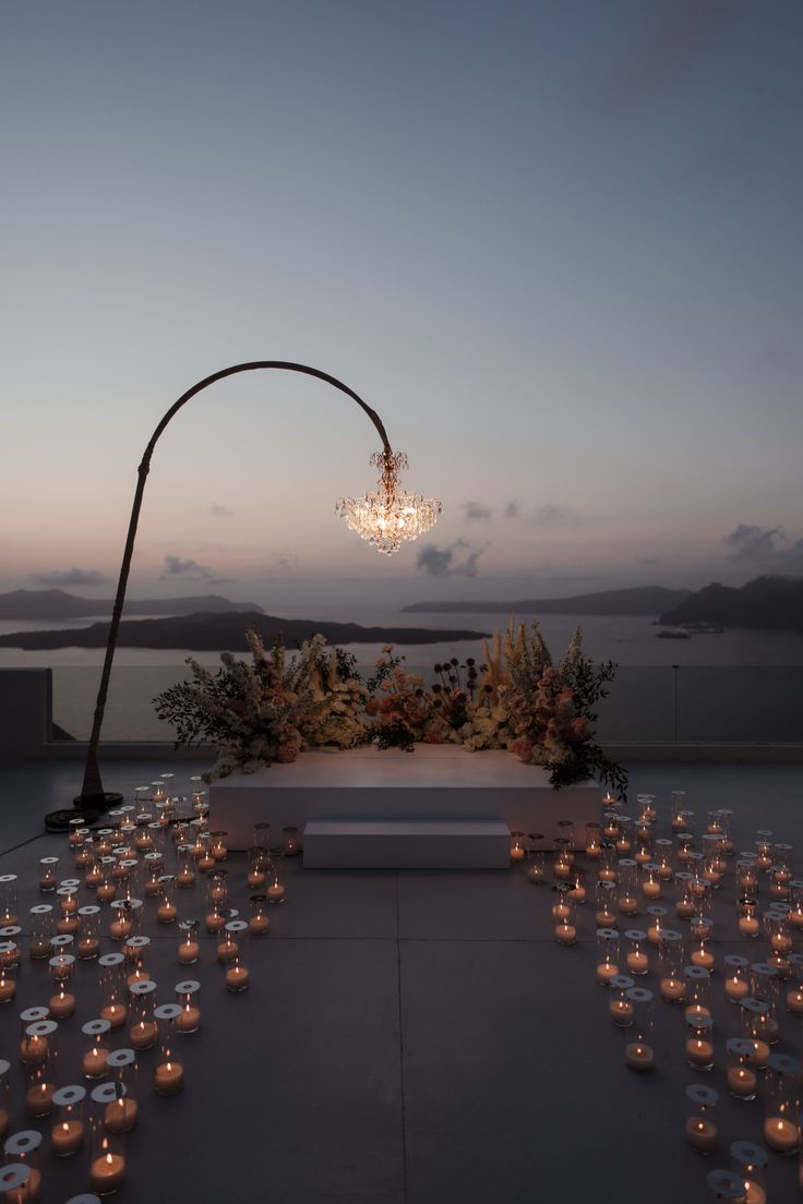 an outdoor ceremony setup with candles and flowers on the ground at dusk, overlooking water