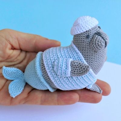 a hand holding a tiny crocheted stuffed animal in a knitted outfit and hat