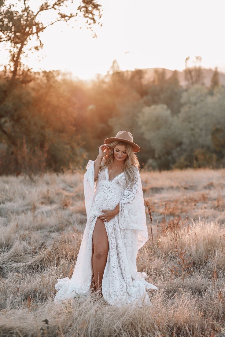 a pregnant woman in a white dress and hat poses for a photo while wearing a cowboy hat