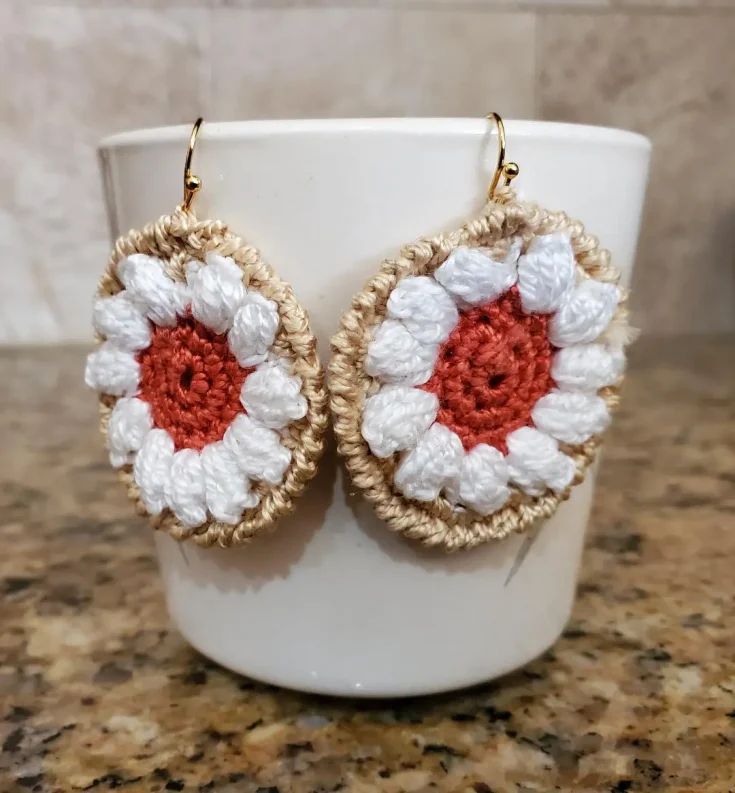 a pair of crocheted flower earrings sitting on top of a white coffee cup