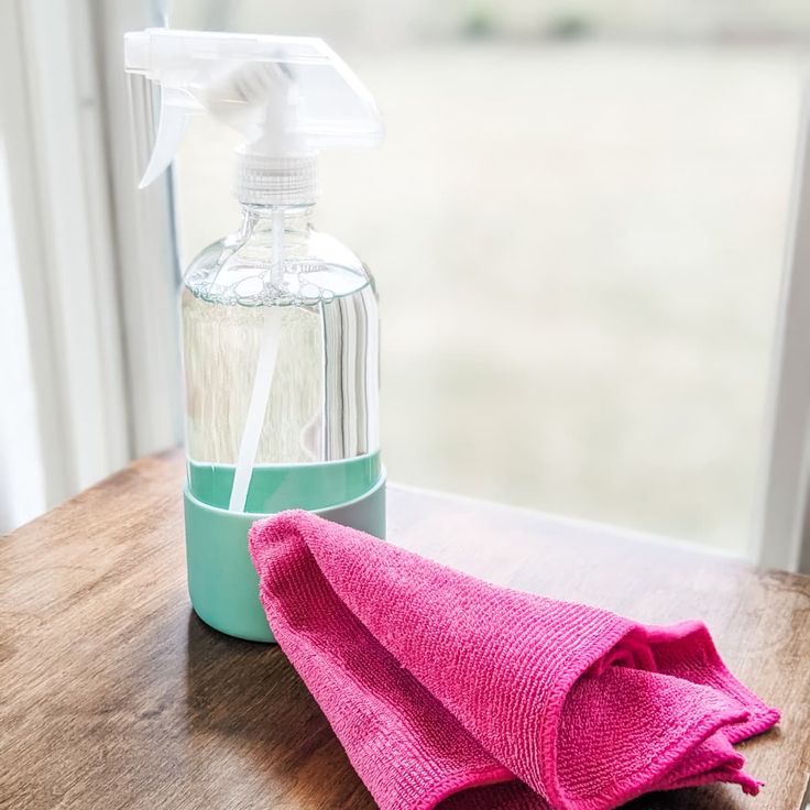 a pink towel sitting on top of a wooden table next to a bottle of cleaner