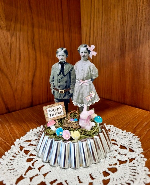 two figurines are standing on top of a cake plate with an easter decoration