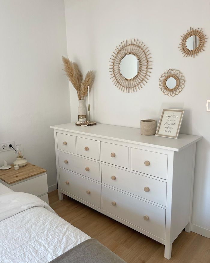 a white dresser sitting next to a bed in a room with two mirrors on the wall