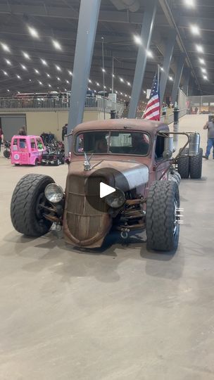 an old car is on display in a building with other cars and people around it