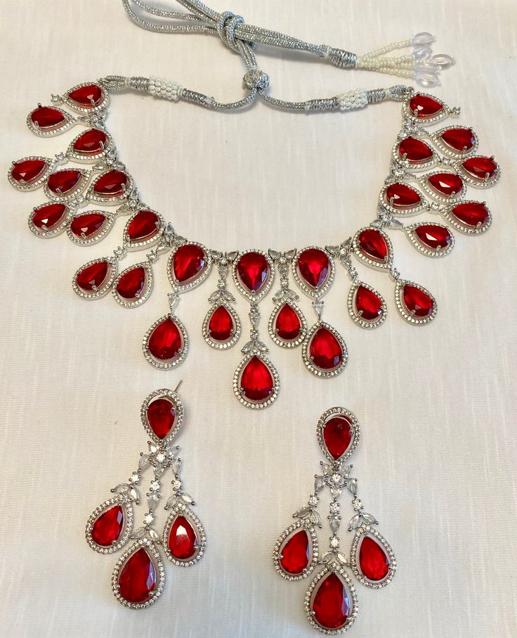 Enhance your jewelry collection with our CZ American Diamond and Red Stone Necklace set. This elegant set is perfect for any party or special occasion. The combination of CZ diamonds and red stones adds a touch of sophistication and glamour. Up your style game and stand out from the crowd with this stunning necklace set. Jewellery Care- Keep the jewellery dry, avoid contact with perfumes and water. Red Party Jewelry With Jewels, Red Crystal Necklaces For Celebrations, Elegant Jeweled Red Bridal Necklace, Elegant Red Jeweled Bridal Necklace, Dazzling Ruby Necklace For Party, Elegant Red Rhinestone Necklaces, Red Crystal Jewelry Sets For Valentine's Day, Red Dazzling Jewelry For Celebration, Dazzling Jewelry For Valentine's Day Party