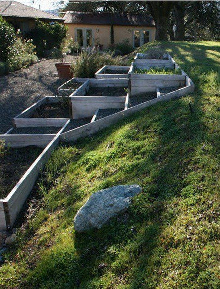 an outdoor garden with raised planters and rocks in the grass next to it on a sunny day