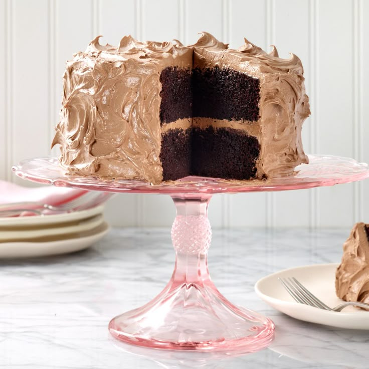 a chocolate cake sitting on top of a glass cake plate with a slice taken out of it