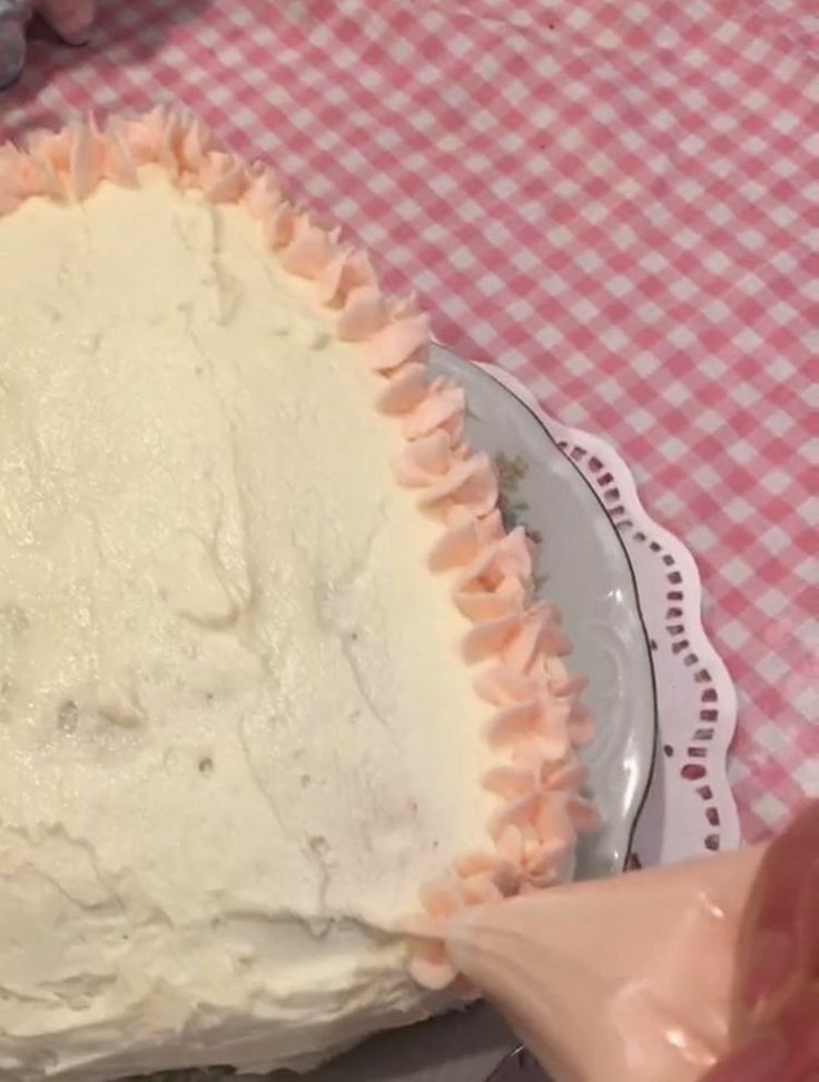 someone is decorating a cake with icing on the plate and pink checkered table cloth