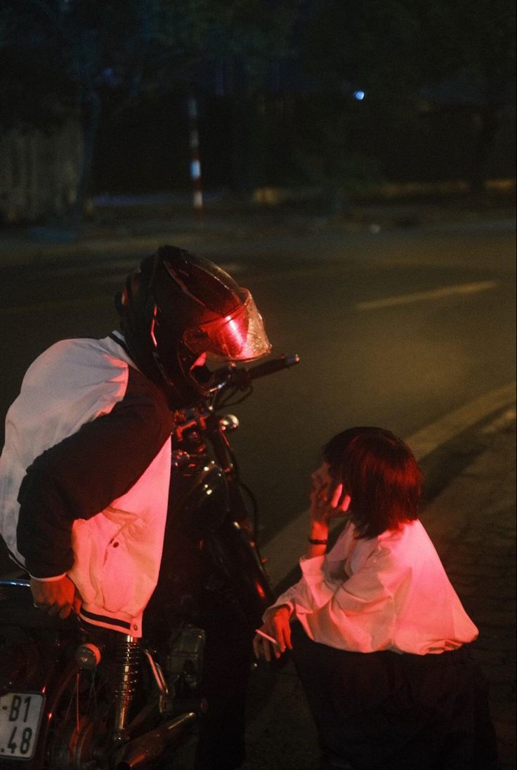 a woman sitting on the back of a bike next to a man talking on a cell phone