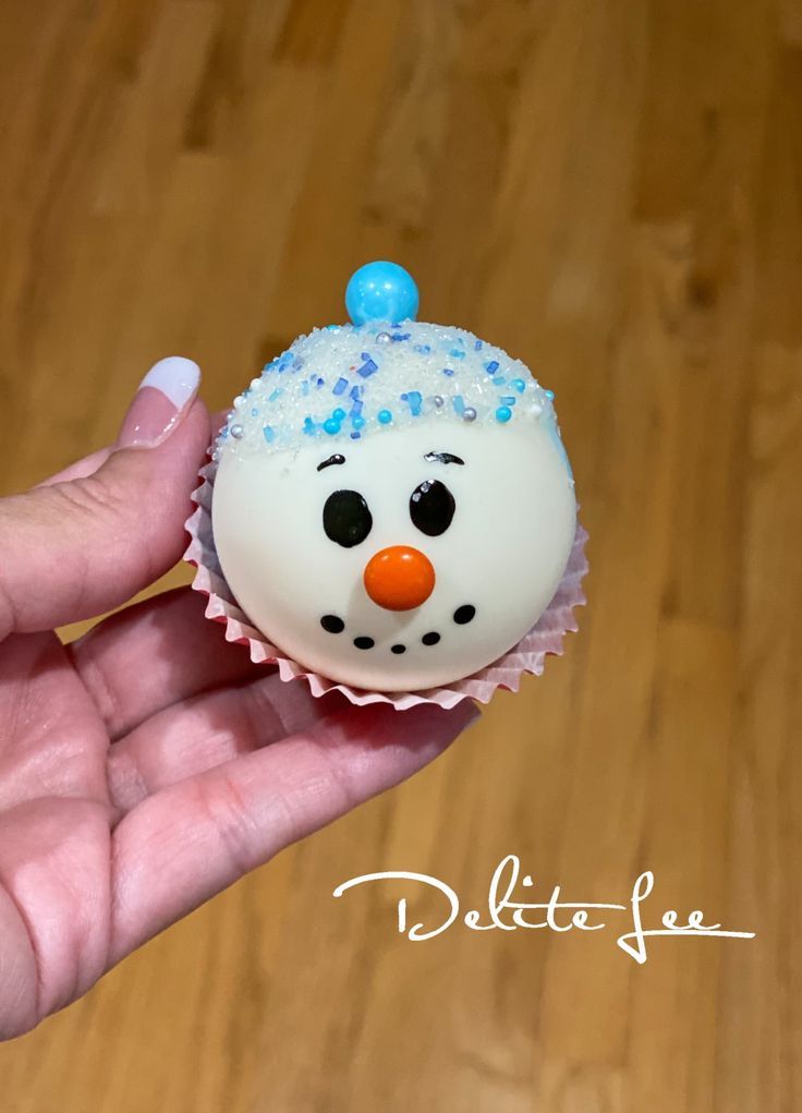 a hand holding a frosted cupcake decorated like a snowman