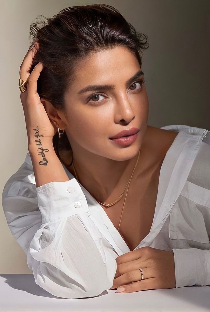 a woman sitting at a table with her hand on her head and wearing a white shirt