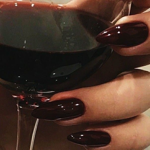 a woman's hand holding a glass of wine with red nail polish on it