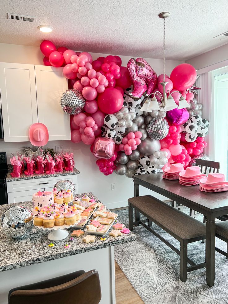 a table with cupcakes, cake and balloons on it in a kitchen area