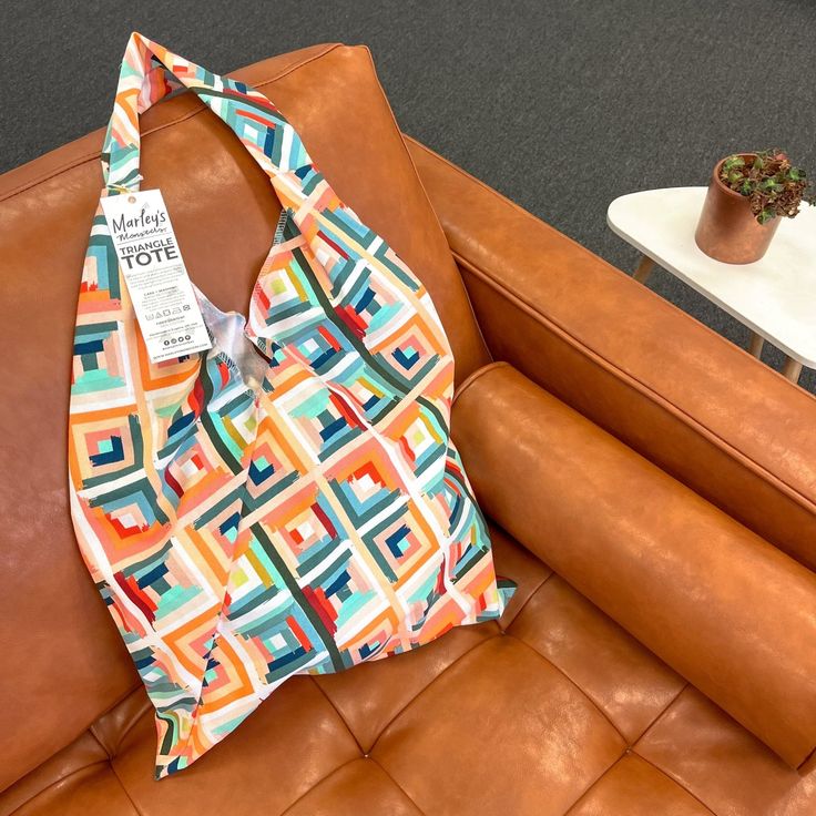 a colorful bag sitting on top of a brown leather couch next to a potted plant