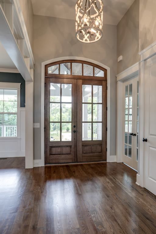 an empty room with wooden floors and two double doors leading to the front door is lit by a chandelier