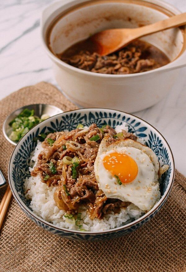 a bowl filled with rice and meat on top of a table next to chopsticks