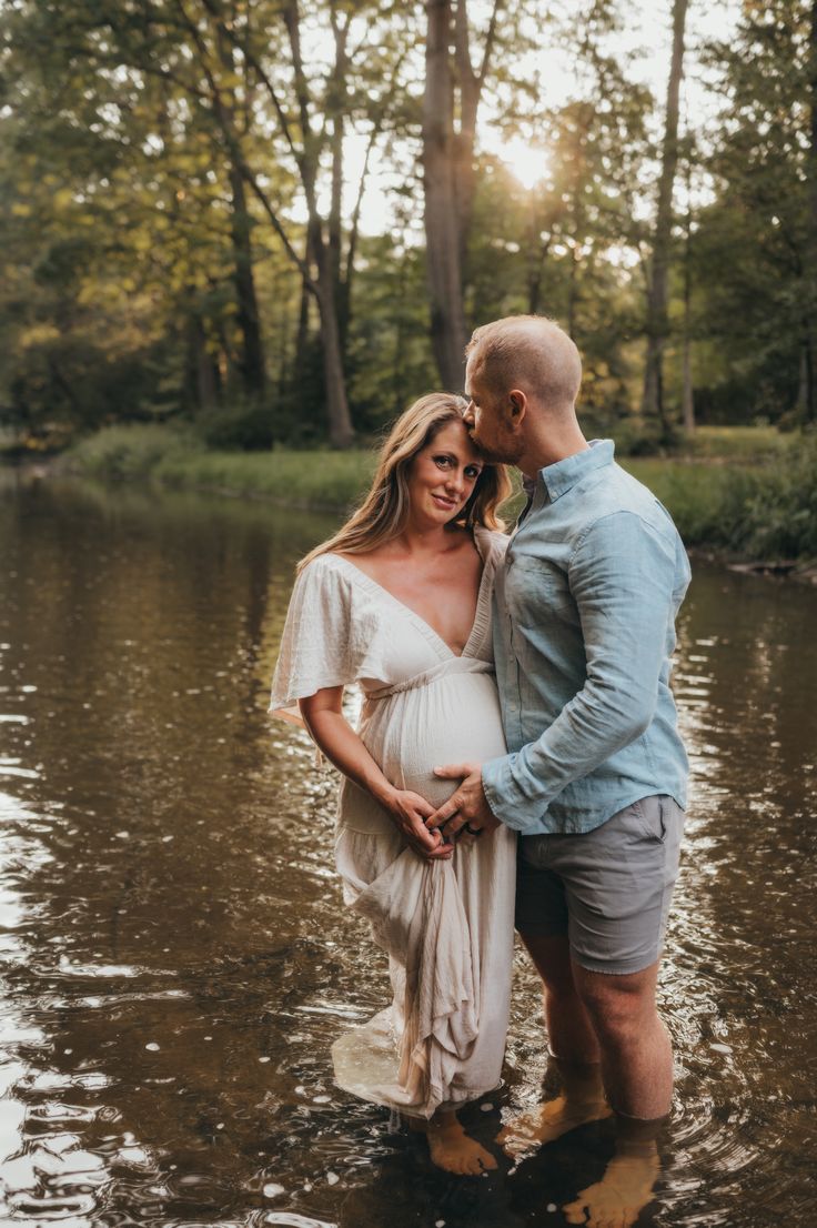 a pregnant couple standing in the water at sunset during their newborn photo session by nature photographer