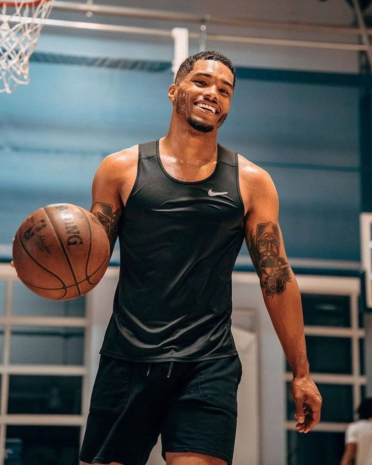 a man holding a basketball while standing in front of a hoop with tattoos on his arm