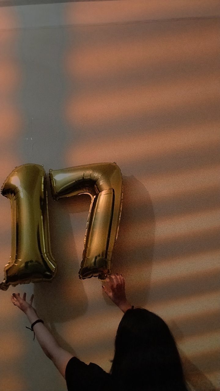 a woman reaching up to the letters f and f on a wall with gold balloons