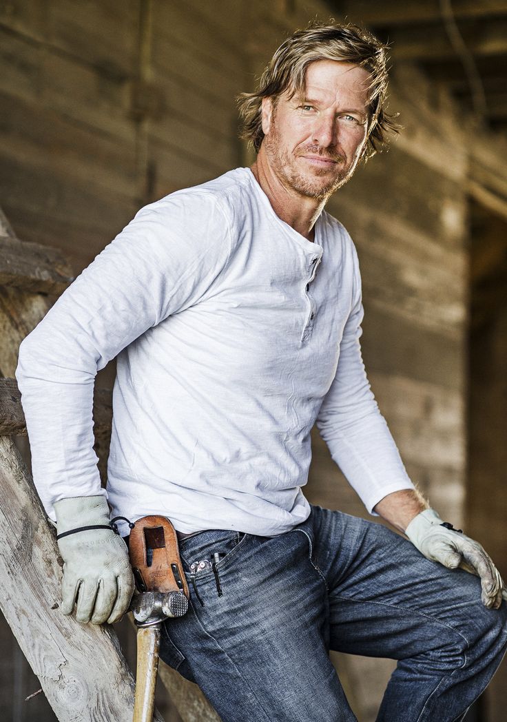 a man in white shirt and jeans holding a skateboard on top of a wooden rail