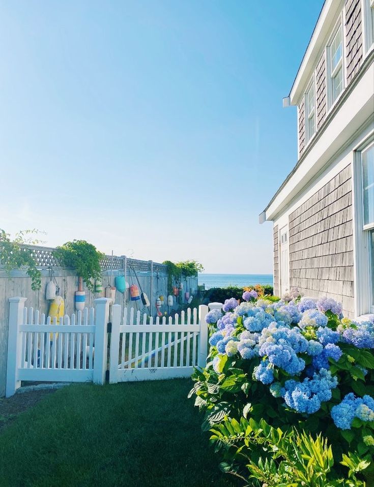 a white picket fence with blue flowers in the foreground and an ocean view behind it