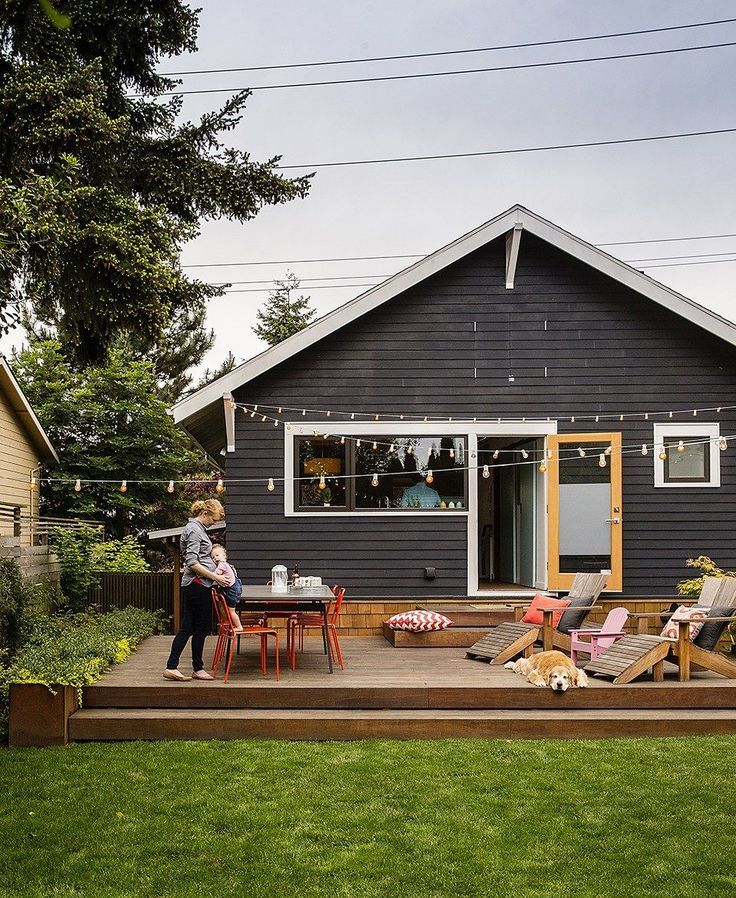 a woman standing on a deck in front of a house with lawn furniture and string lights