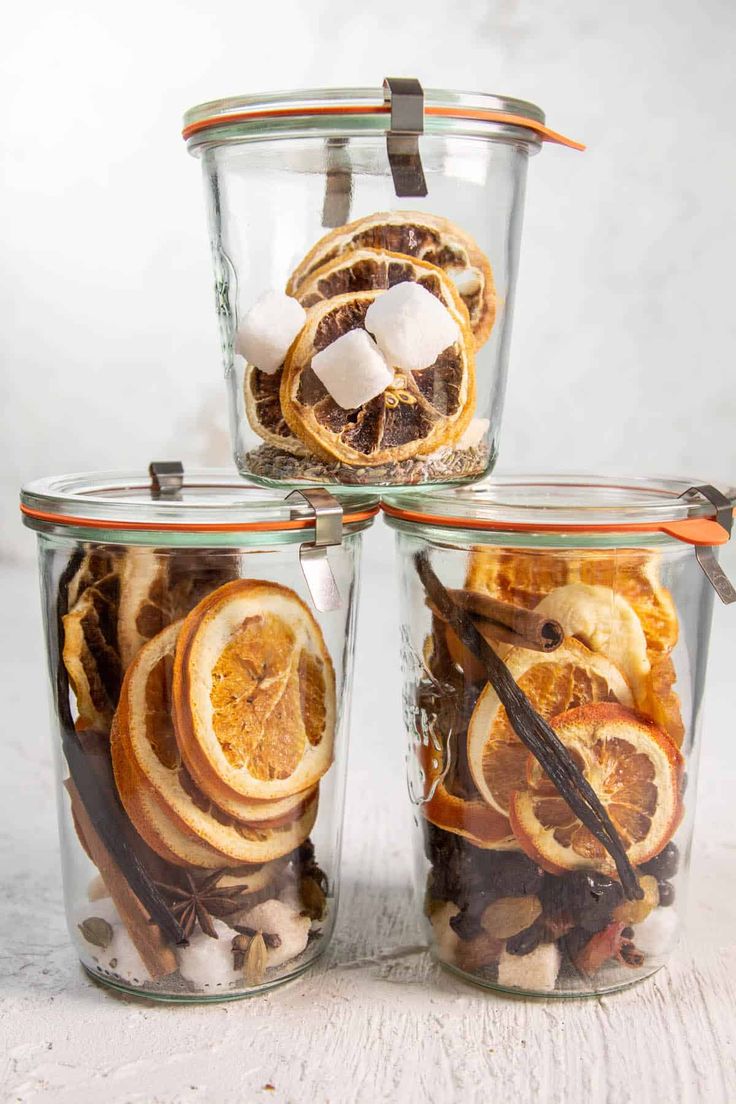 three glass containers filled with orange slices and marshmallows on top of each other