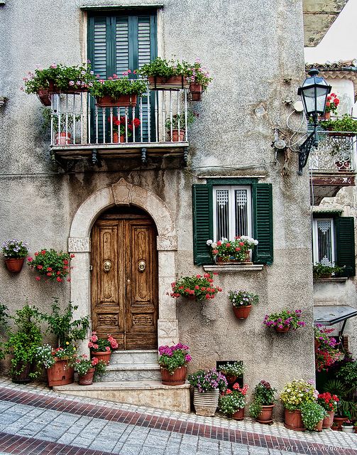 an old building with flowers and potted plants on the front door, windows and balconies