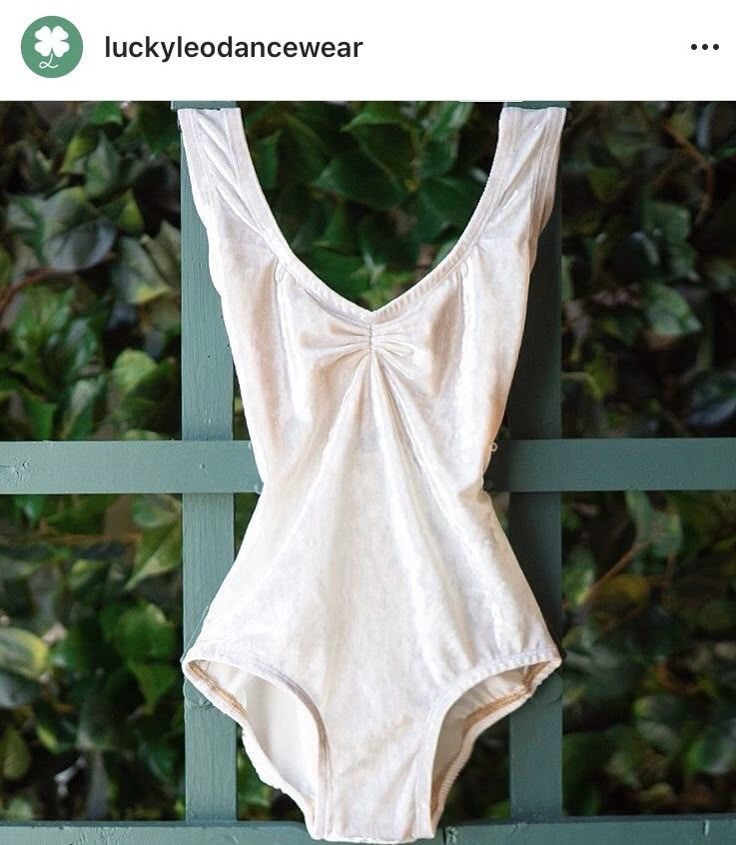 a white one piece swimsuit hanging on a green fence