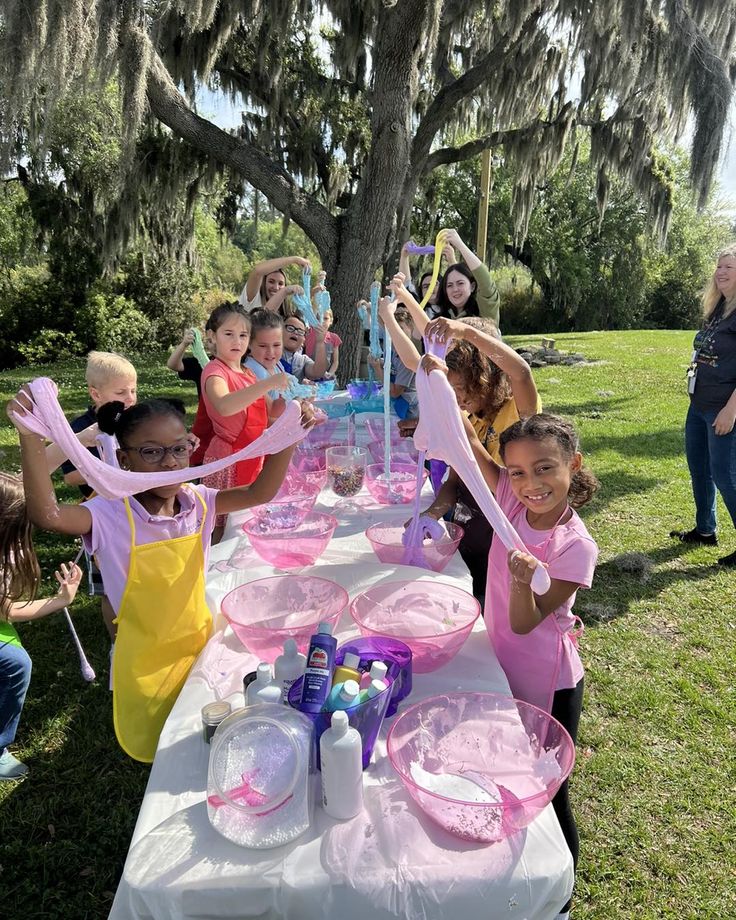 a group of children standing around a table with pink plates and cups on top of it