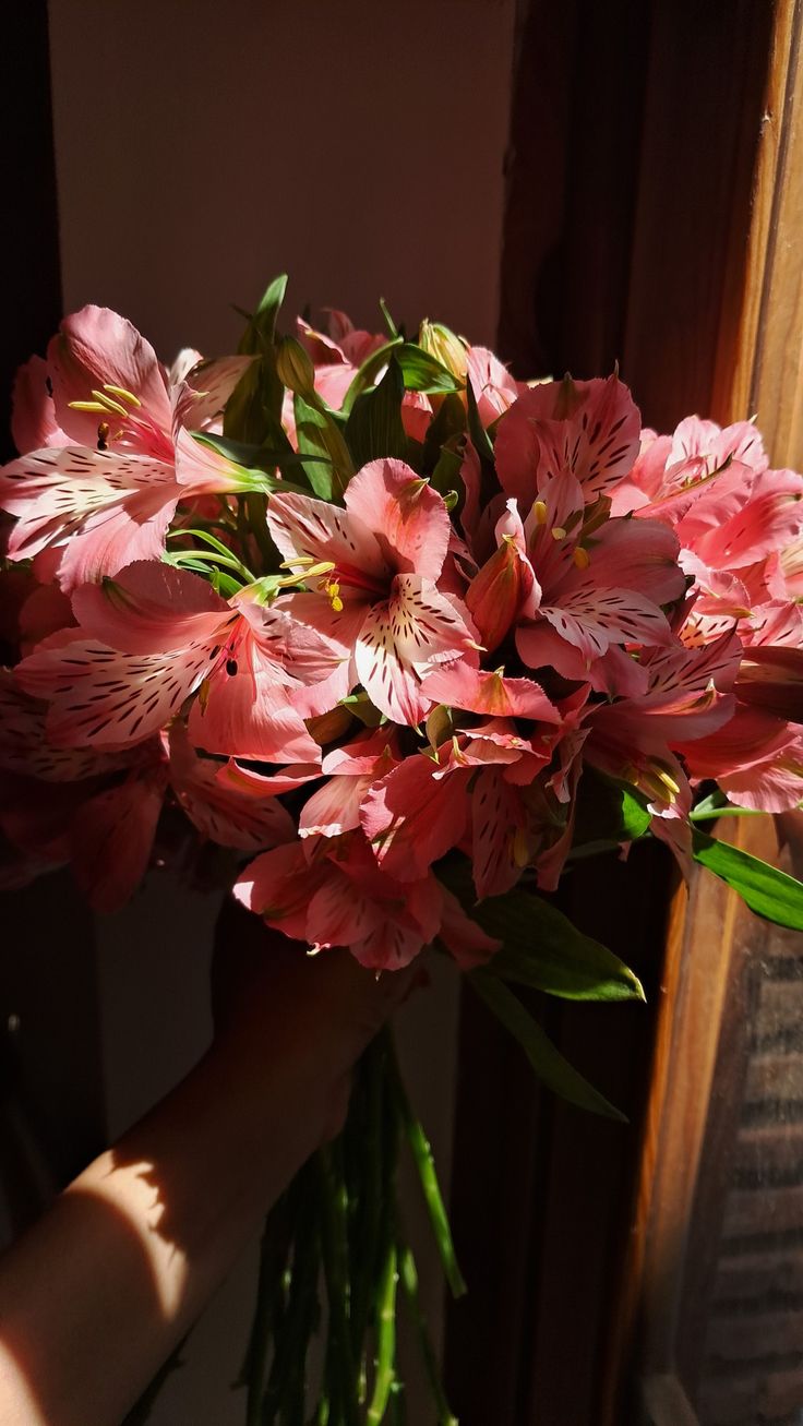 a bouquet of pink flowers sitting on top of a window sill next to a person's hand