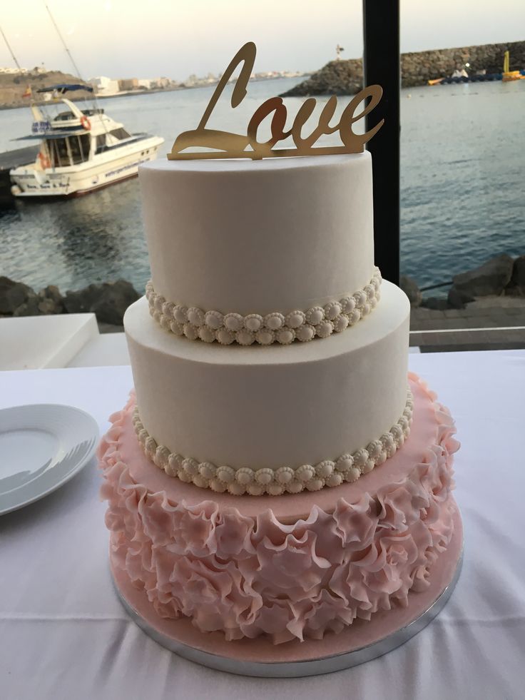 three tiered wedding cake with pink and white ruffles on the table next to water