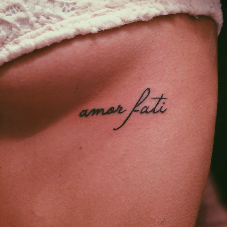 a woman's lower back tattoo with the word amar fati written in cursive font