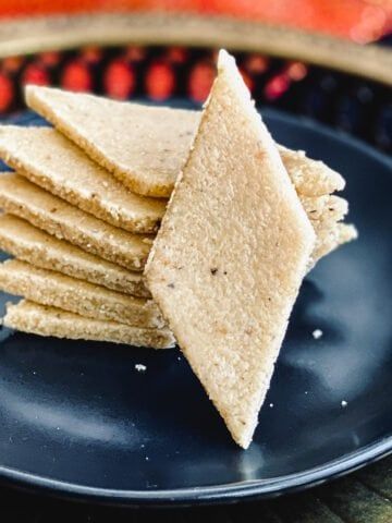 a black plate topped with crackers on top of a wooden table