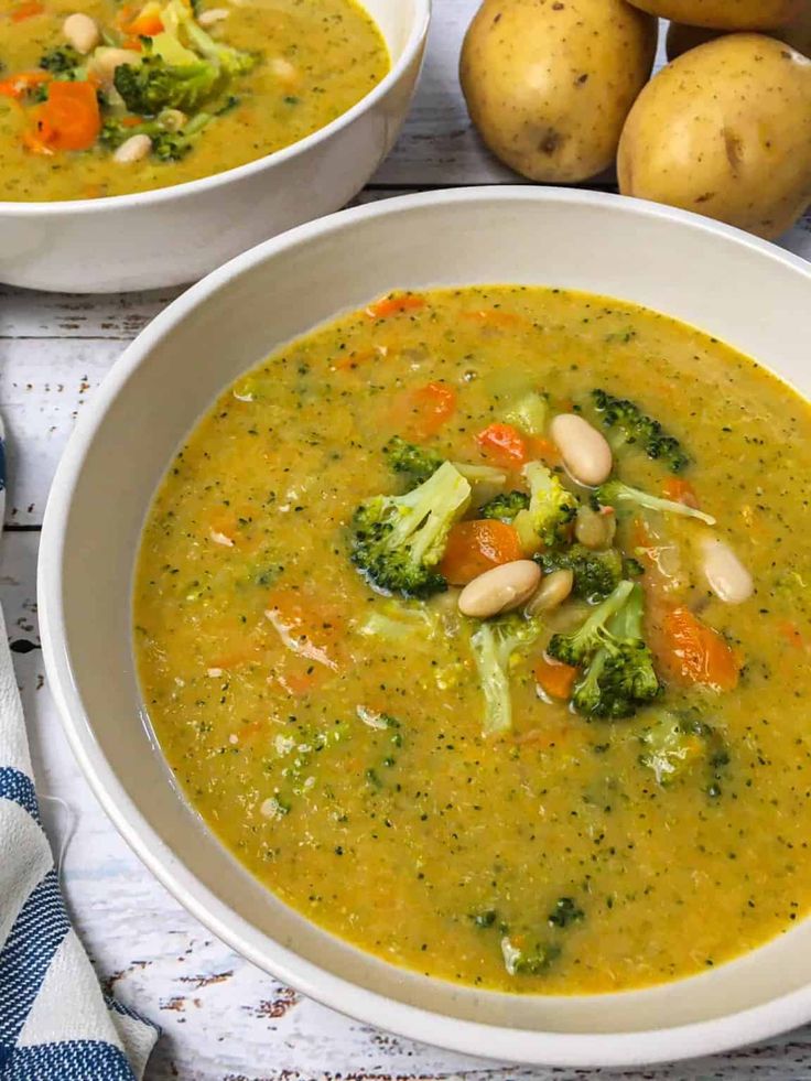 two bowls of soup with broccoli, carrots and potatoes on the side