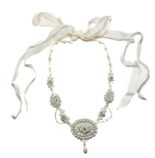 a white scarf tied around a necklace with beads and pearls on it, along with a ribbon