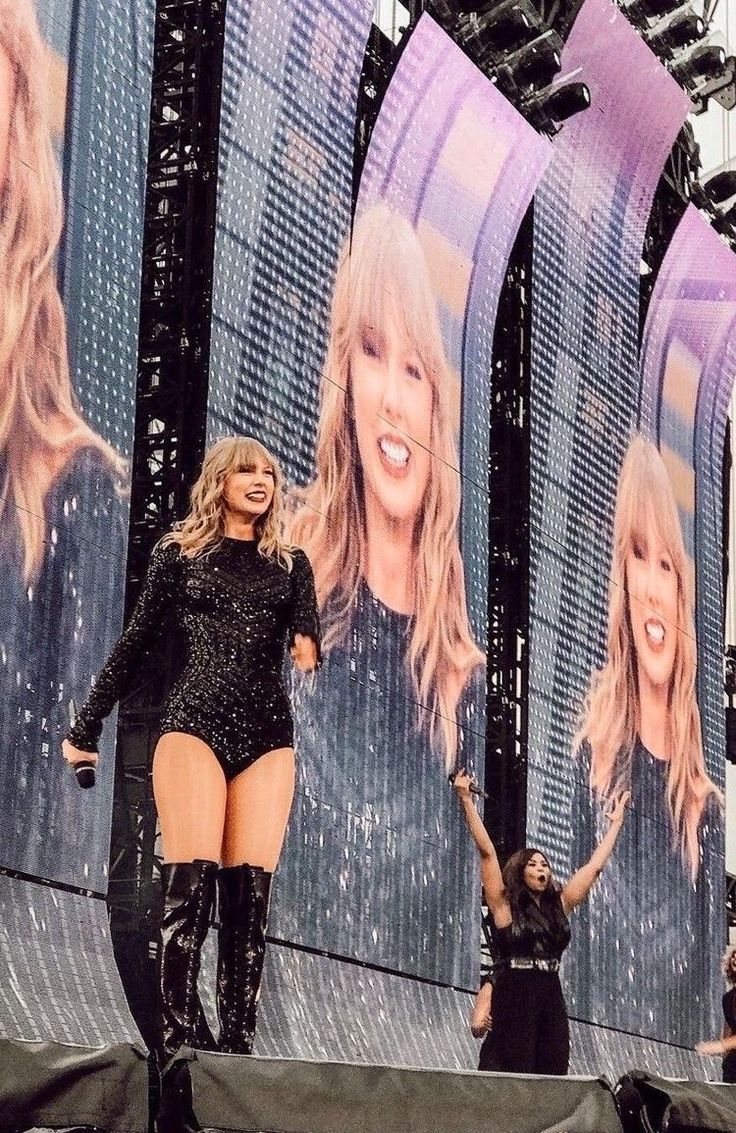 a woman standing on top of a stage in front of a large screen with two women