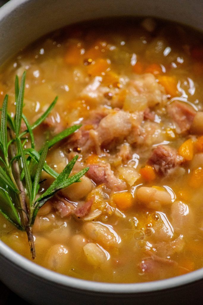 a white bowl filled with soup and meat on top of a wooden table next to a green sprig