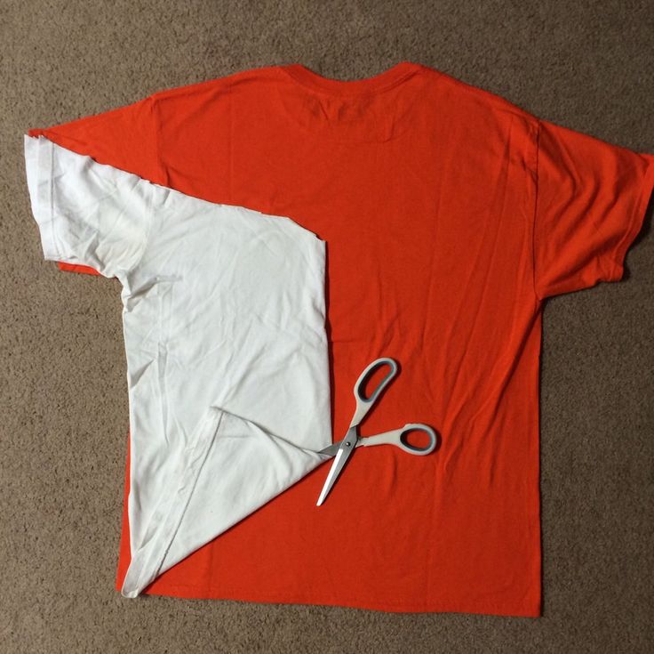 a pair of scissors sitting on top of an orange shirt next to a pair of white t - shirts