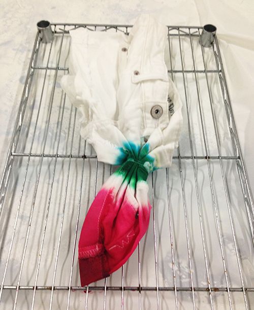 a white jacket and pink flower laying on a wire rack next to some cloths