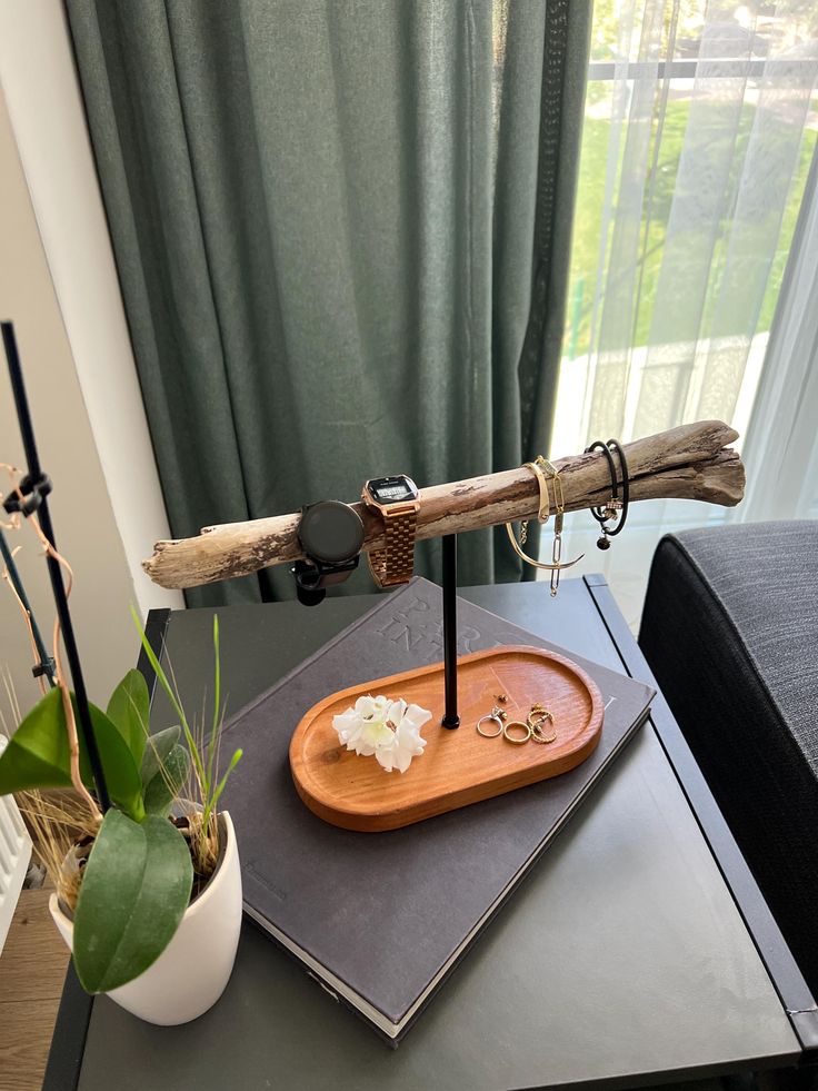 a wooden tray with two rings on top of it next to a plant and window