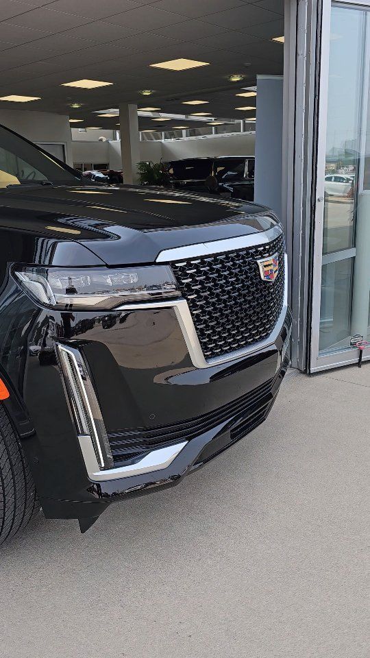 a black cadillac parked in front of a car dealership with it's door open