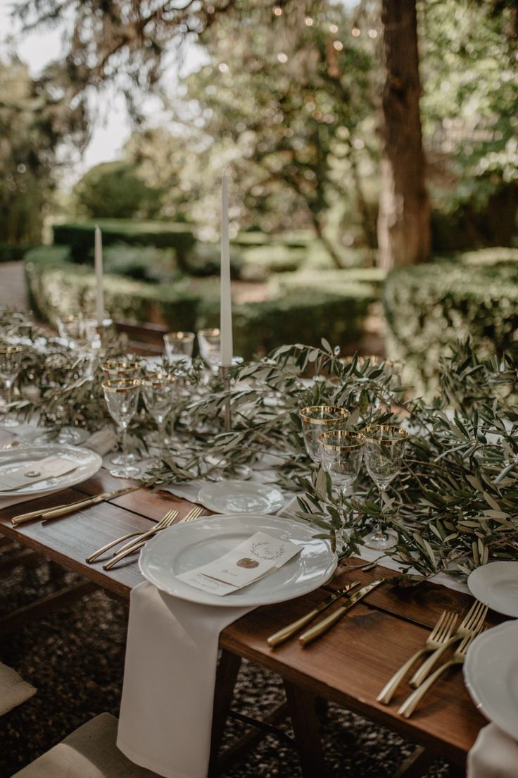 the table is set with white plates and silverware for an elegant outdoor dinner party